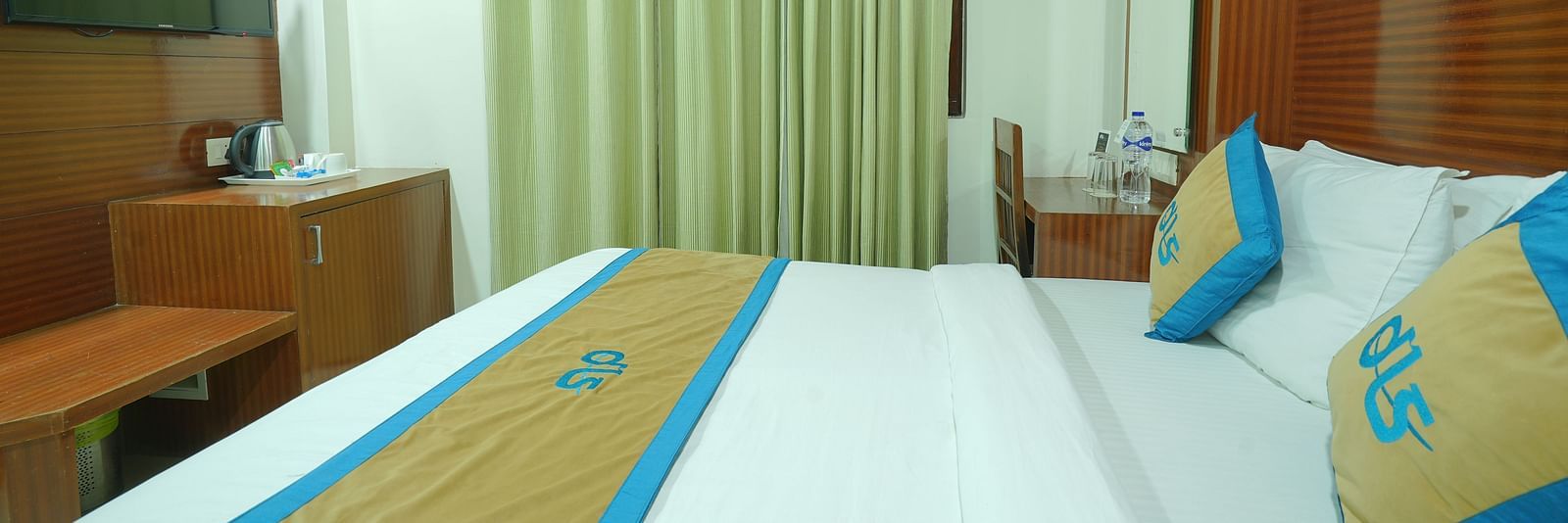 Side view of a deluxe room featuring a king size bed, a television, and a window covered by curtains at DLS Hotels The Rock Castle.